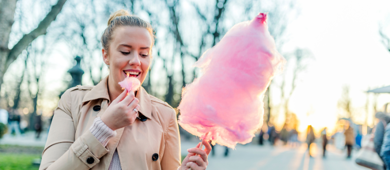 Lachende vrouw eet een roze suikerspin in een park bij zonsondergang.