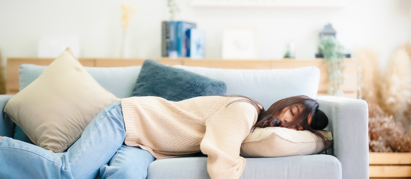 Vrouw ligt te slapen op een blauwe bank in een moderne woonkamer.