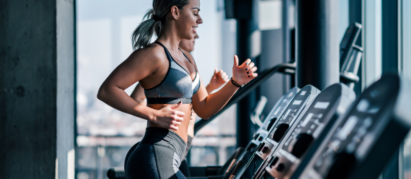 Vrouw traint op een loopband in een fitnesszaal, geconcentreerd op haar workout.