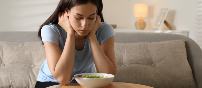 Vrouw kijkt naar een kom salade, twijfelend of ze het zal eten, in een woonkamer.