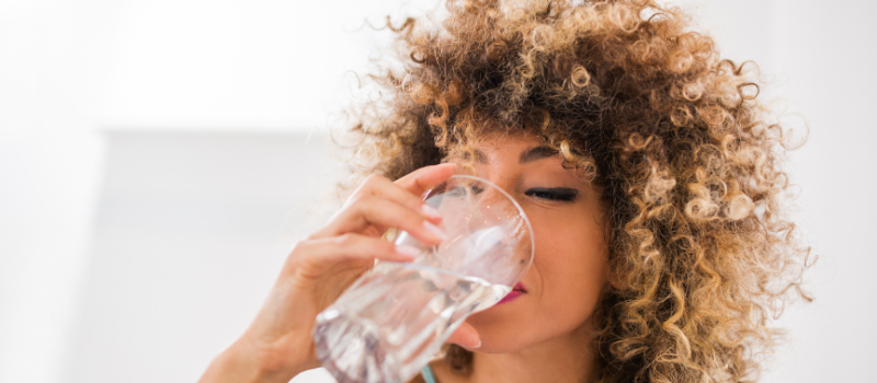 Vrouw drinkt een glas water, hydratatie en gezondheid.