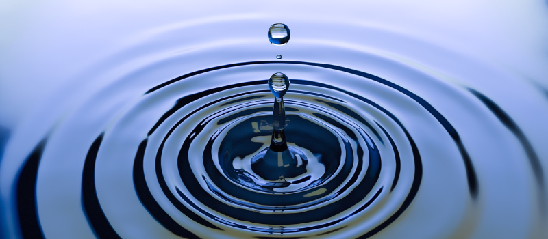 Vallende waterdruppel met concentrische golven, wateroppervlak