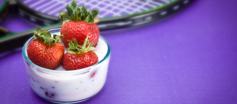 Kom yoghurt met verse aardbeien naast tennisracket, sport en snack