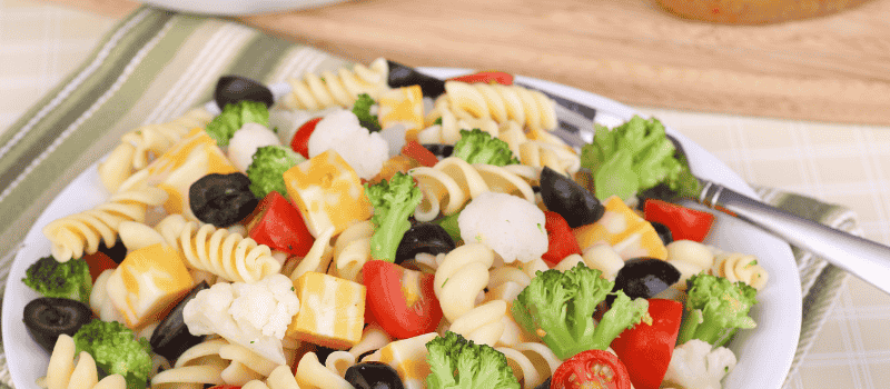 Een kleurrijke pastasalade met broccoli, tomaten, kaasblokjes, zwarte olijven en bloemkool.