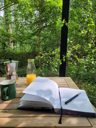 Houten tafeltje in het bos met daar op een dagboek en vulpen, koffie en fruitsap. Heerlijk ontspannen.