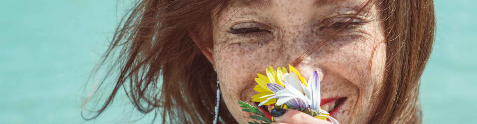 Vrouw met sproetjes lacht en ruikt aan bloemen