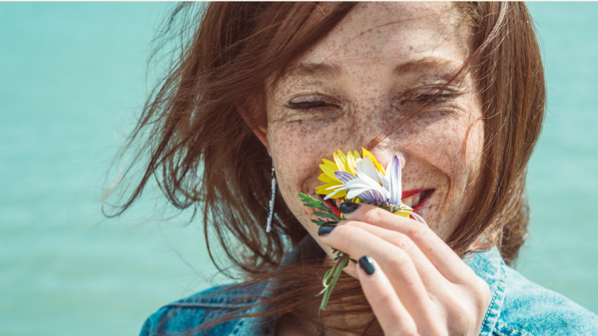 Vrouw met sproetjes lacht en ruikt aan bloemen