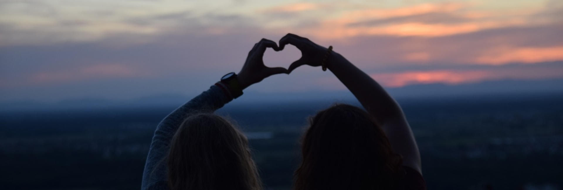 vrouwen maken hartje met handen bij zonsondergang