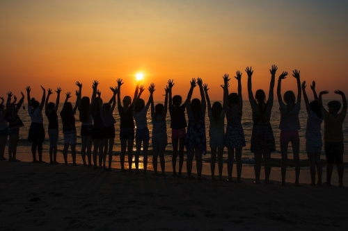 groep mensen staat met handen omhoog op het strand bij zonsondergang