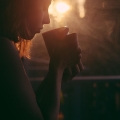 Vrouw drinkt koffie voor een raam met de opkomende zon