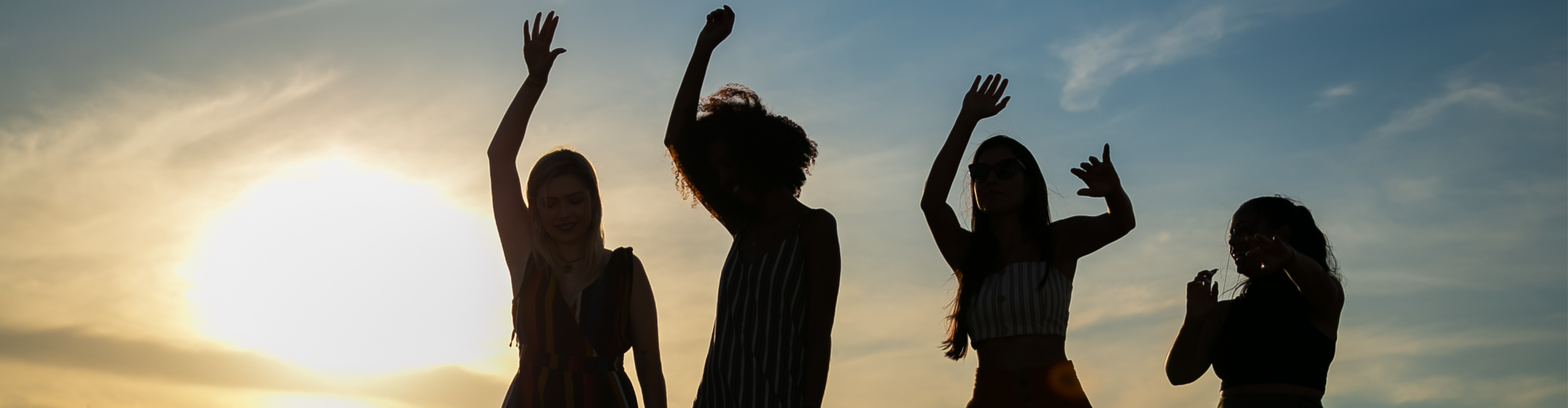 Vier vrouwen dansen. Door de zon achter hen zie je enkel hun silhouet.