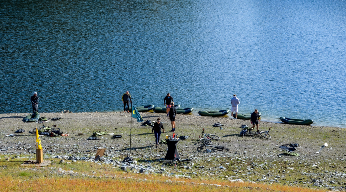 Team tijdens een pauze aan de Rursee tijdens een bikeraft teambuilding van YALPAK in de Eifel, met packrafts en mountainbikes op de oever.
